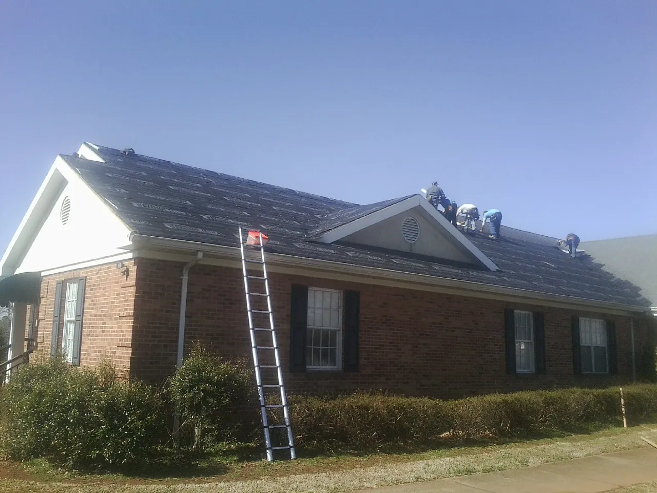 Crew tearing shingles off a brick ranch roof with a ladder set — Emergency Roof Repair work by our crew in Bethel Island