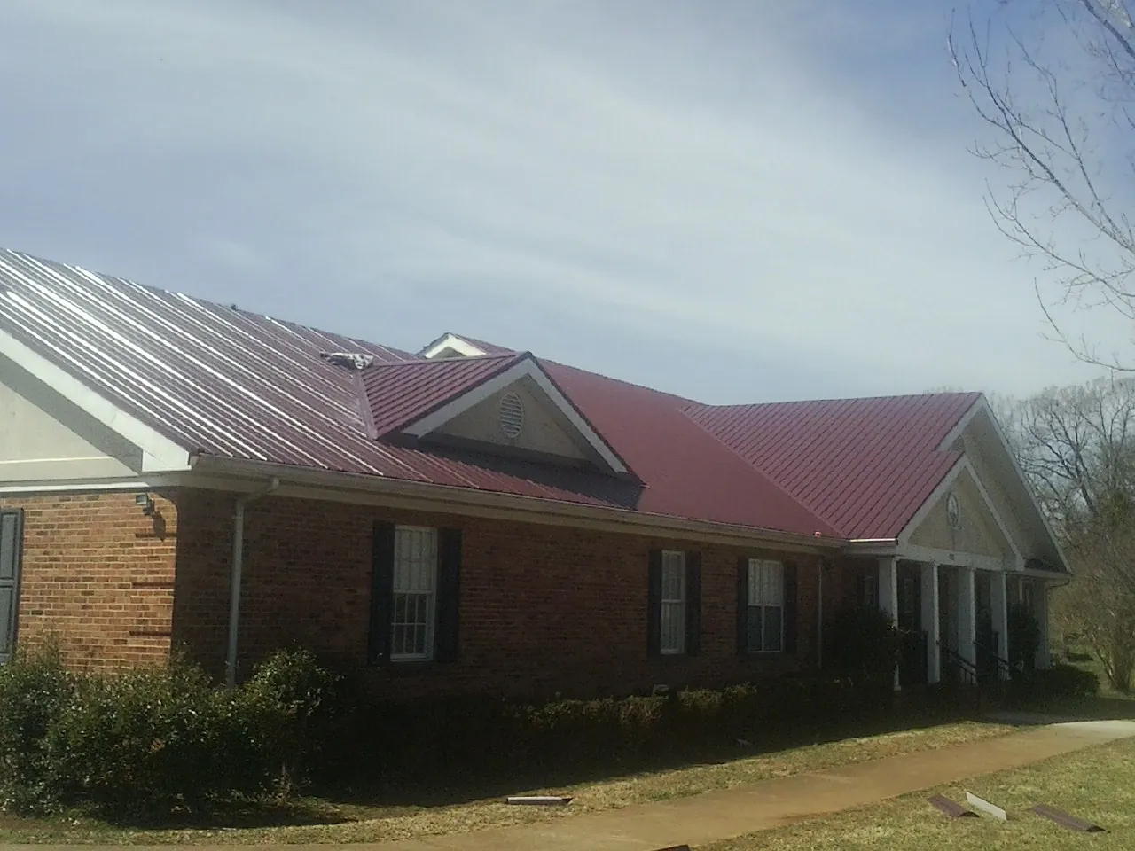 Red metal roof with gabled entries on a long brick building, from a Hail Damage Roof Repair job in Bethel Island