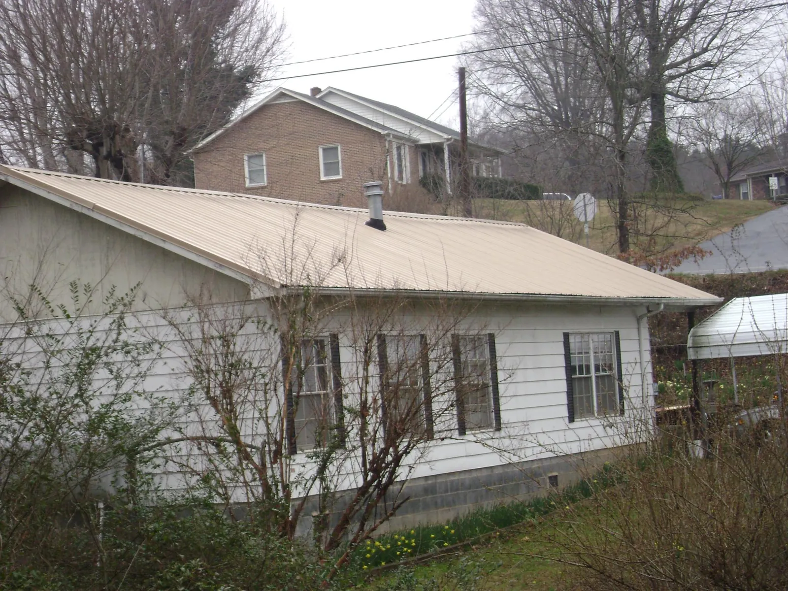 Tan metal roof on a white sided house set into a hillside — Commercial Roofing by Roofing Brothers in Bethel Island